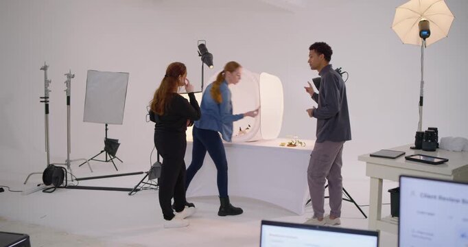 Photography crew planning positions and opening light tent in studio product shoot, arranging props