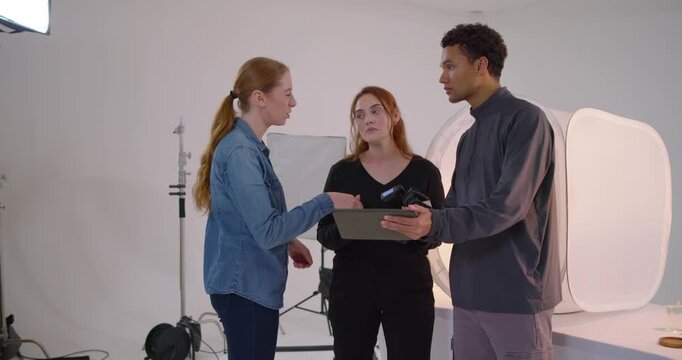 Studio team reviewing tablet, placing props in light tent, adjusting lamp for product shoot