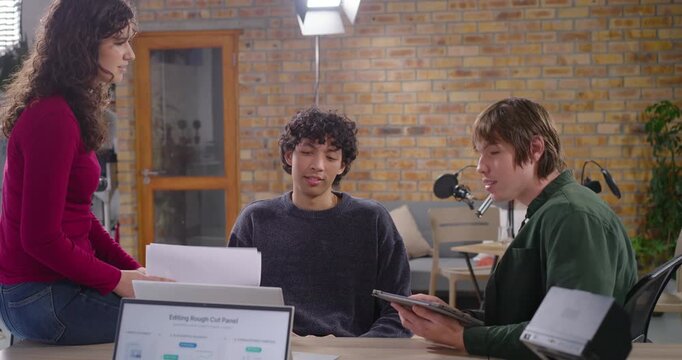 Colleagues editing while woman approaching with pages, placing them and checking tablet with laptop