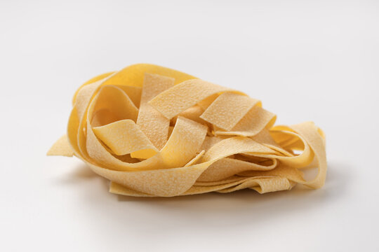 Italian dry fettuccine or tagliatelle pasta over white background with shadow
