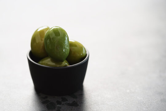 big green olives in black bowl on concrete background