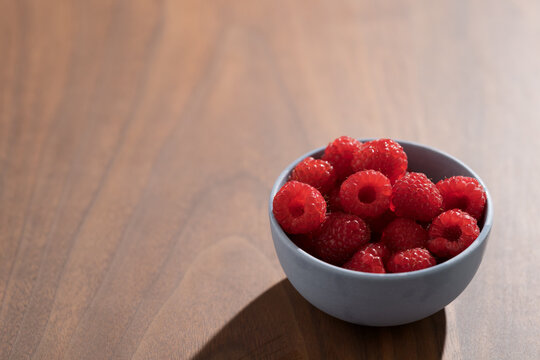 Bowl of fresh washed raspberries on walnut wood table with copy space