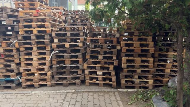 Stacks of wooden pallets stored outdoors beside a building, industrial storage, logistics equipment, shipping materials, warehouse yard