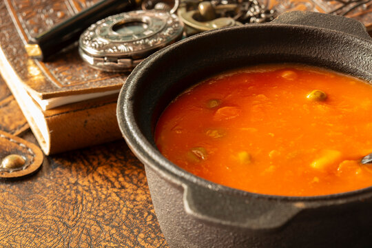 Bowl of vegetable soup with a vintage leather journal, fountain pen and a pocket fob watch on an aged leather background backdrop