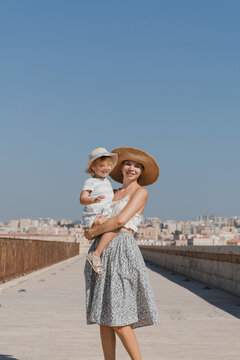 Smiling mother holding her laughing child on a sunny city bridge