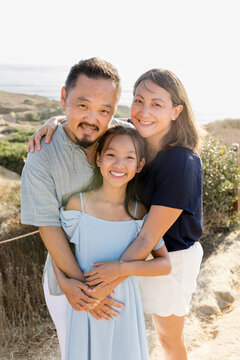 Happy Asian family of three hugging outdoors