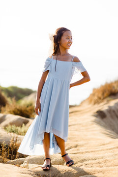 Happy young girl in a blue dress stands on a sunny trail