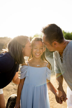 Affectionate parents kissing their smiling daughter's cheeks