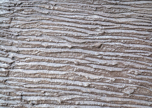 Gray and brown surface with irregular parallel ridges, shallow grooves, and a layered linear texture.