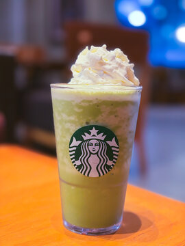 Bangkok, Thailand - October 10, 2026: Close up of a Starbucks matcha green tea frappuccino topped with whipped cream on a wooden table in a cafe.