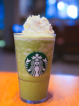 Bangkok, Thailand - October 10, 2026: Close up of a Starbucks matcha green tea frappuccino topped with whipped cream on a wooden table in a cafe.