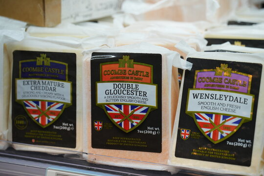Assorted packaged traditional British cheeses are displayed on a shelf.