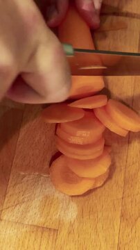 Hands Slicing a Carrot Into Rings on a Wooden Board