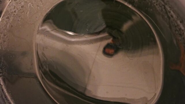 Single red garment tumbling inside a spinning washing machine drum seen through the round glass door, close up of colored laundry in motion, concept of separating colors, sorting clothes and avoiding