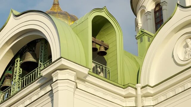 Church bells hang and chime under green arched roofs. Their heavy clappers strike metal, creating a clear and solemn ringing sound across the town.