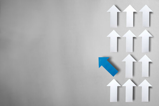 Paper blue arrow pointing in a different direction from white arrows with copy space. concepts of unconventional thinking, standing out, business strategy, and driving change.