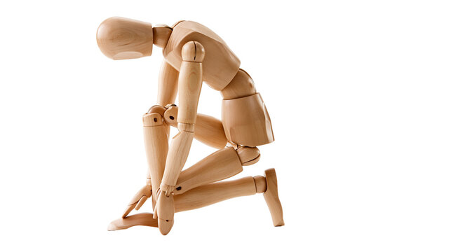 Wooden articulated mannequin figure kneeling in a sad or depressed posture