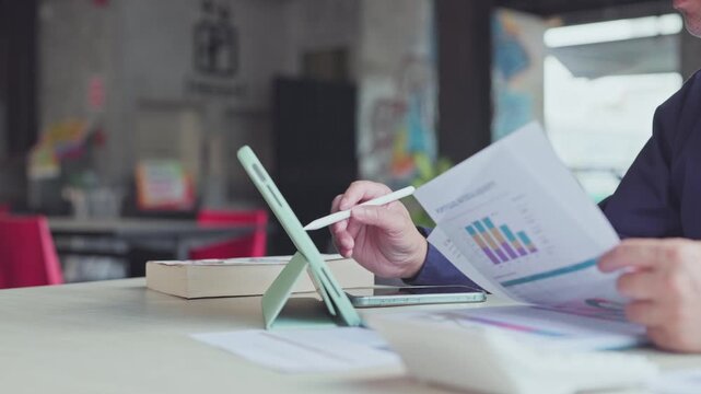 Professional accountant analyzing financial report paperwork holds digital pen touching tablet screen on office desk.