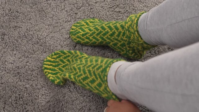 Close up of woman feet in green knitted wool socks on living room floor, representing winter season, warmth and cozy home atmosphere.