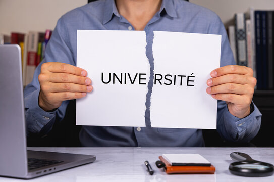 Une personne en chemise tenant une feuille de papier d&eacute;chir&eacute;e sur laquelle est &eacute;crit en gros le mot universit&eacute;.
