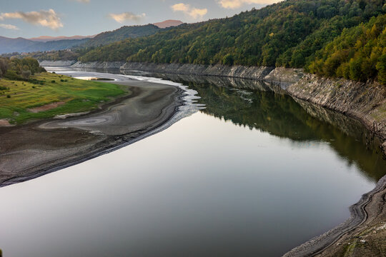 Wide view of the Nestos river winding through a valley with exposed dry cracked mudbanks reflecting the surrounding autumn forest hills due to low water levels in Greece.