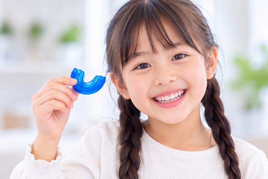 青い小児矯正用マウスピースを手に持って笑顔を見せる日本人の女の子