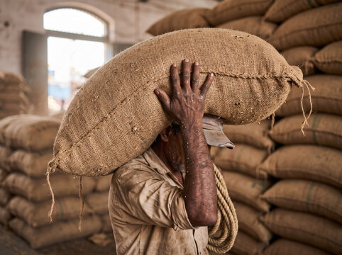 Harbour porter carrying a heavy burlap sack of green coffee beans with copy space for agricultural trade and global supply chain concepts.