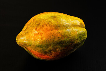 Fototapeta premium Black background featuring whole ripe papaya with yellow green and orange skin texture tropical fruit