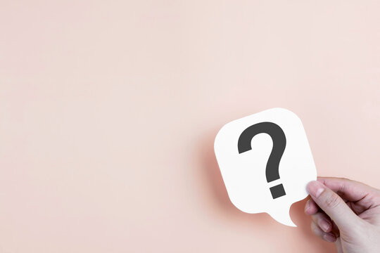 A hand holding a speech bubble with a question mark against a pastel background, representing concepts of FAQs, problem solving, decision making, and customer consultation services.