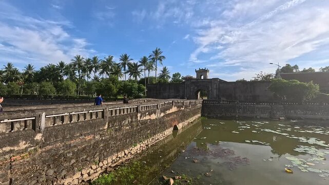 Tourists walking on the stone bridge over the moat towards the gate of Quang Tri Ancient Citadel in Vietnam.