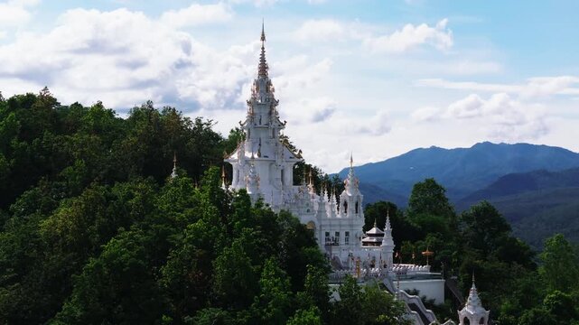 Aerial approach to a white temple on a forested mountain ridge