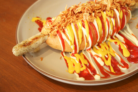 Gourmet German sausage hot dog topped with crispy onions and drizzled sauces on a plate
