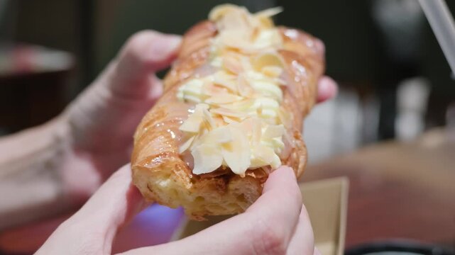 Close-up of a person holding a fresh baked almond puff pastry braid with cream and flaked almonds in a bakery or cafe. Sweet dessert, confectionery and bakery products concept.