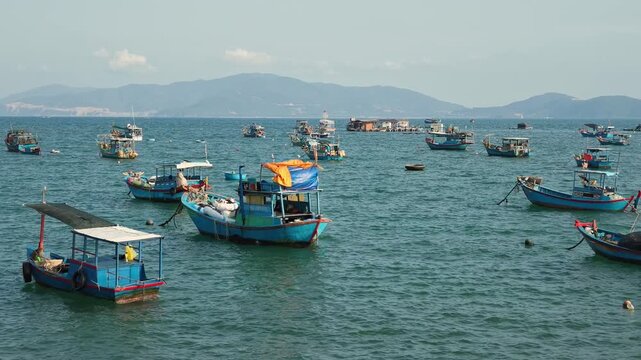 Scenic panoramic view of traditional wooden fishing boats anchored in the sea bay against modern city skyline of Nha Trang, Vietnam. Travel, coastal cityscape and tourism concept.