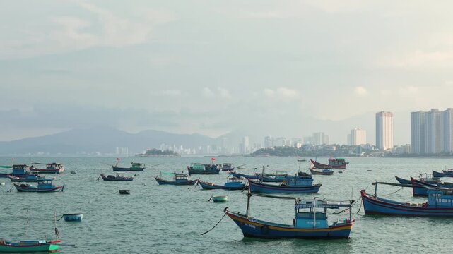 Scenic panoramic view of traditional wooden fishing boats anchored in the sea bay against modern city skyline of Nha Trang, Vietnam. Travel, coastal cityscape and tourism concept.
