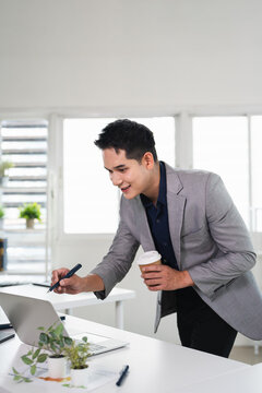 Young asian professional business man working on laptop, remote working using computer looking at screen watching seminar or searching information at office.