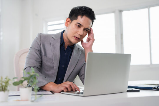 A stressed businessman experiences financial crisis, bank debt. Man sitting at desk holding receipt or financial report feels desperate .