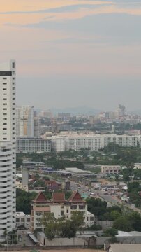 Vertical aerial view of modern skyscraper and Pattaya city valley at sunset, Thailand. Drone shot of tall apartment building, urban streets and tropical cityscape in evening, travel concept.