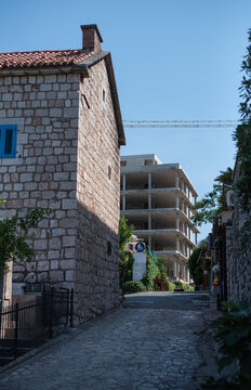 Narrow cobblestone street in Sveti Stefan, Montenegro, runs between an old stone house and a modern concrete building under construction