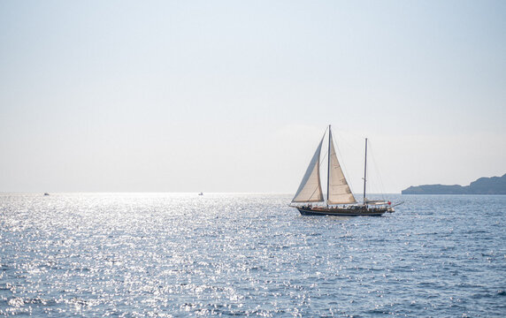 Wooden two-masted sailboat sails across the sparkling blue sea on a bright sunny day