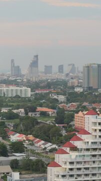 Vertical aerial view of modern skyscraper and Pattaya city valley at sunset, Thailand. Drone shot of tall apartment building, urban streets and tropical cityscape in evening, travel concept.