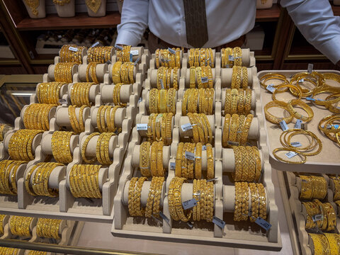 Rows of gold bangles filling a display stand behind a jeweller counter in the gold souk of Deira, Dubai, United Arab Emirates