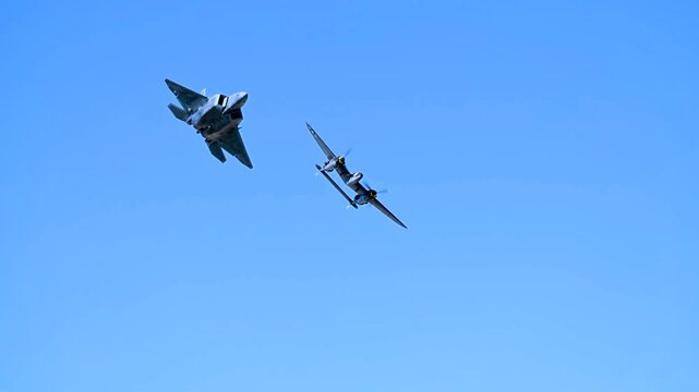 An F-22 Raptor and a Vintage P-38 Lightning Fighter Jet Flying in Formation Against Sky.