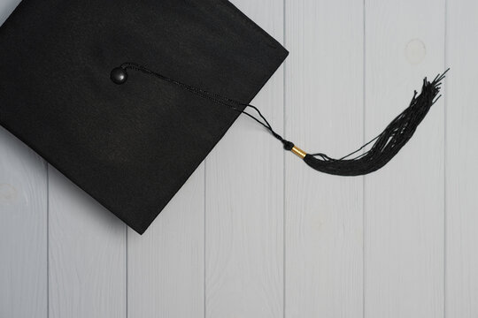 Black graduation cap with tassel symbolizing education learning and accomplishment on light wood background