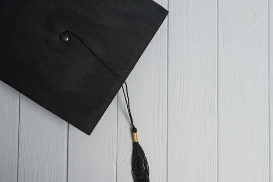 Black graduation cap with tassel symbolizing education learning and accomplishment on wood background a light