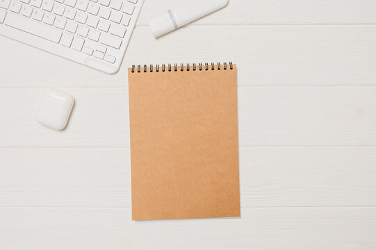 Brown craft mockup notebook and wireless earbuds on white desk composing workspace concept top view