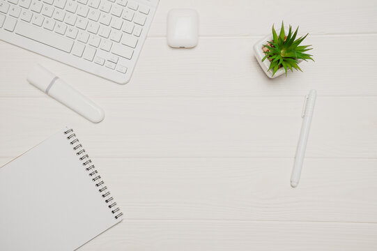 White minimal office workspace flat lay with modern wireless keyboard earbuds and notepad wooden desk on clean