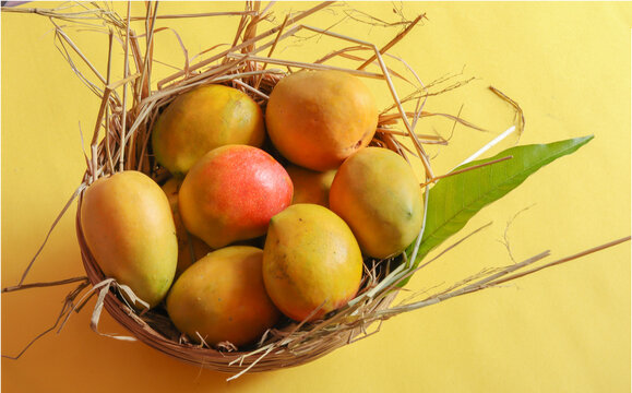 A basket of vibrant Indian mangoes, showcasing rich shades of yellow, orange and red with fresh green leaves against a warm background.