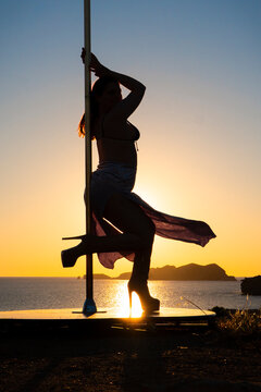 White woman performing pole dance silhouette at sunset in Ibiza, Spain