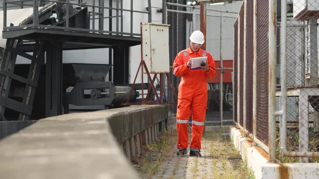 Engineer walks through industrial facility while checking documents near electrical transformer enclosure. Power infrastructure inspection, equipment maintenance, workplace safety assessment.